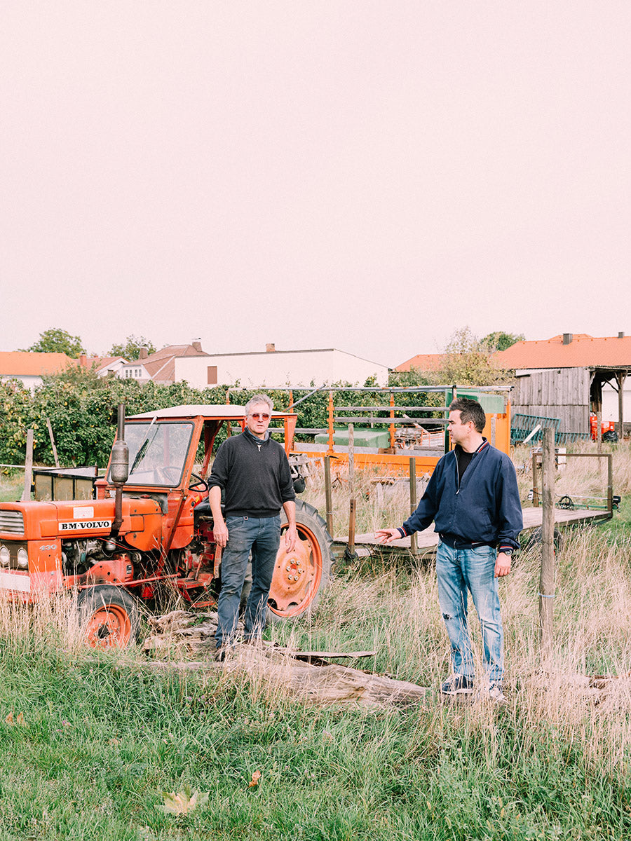 zwei Personen vor einem orangenen Traktor auf Wiese